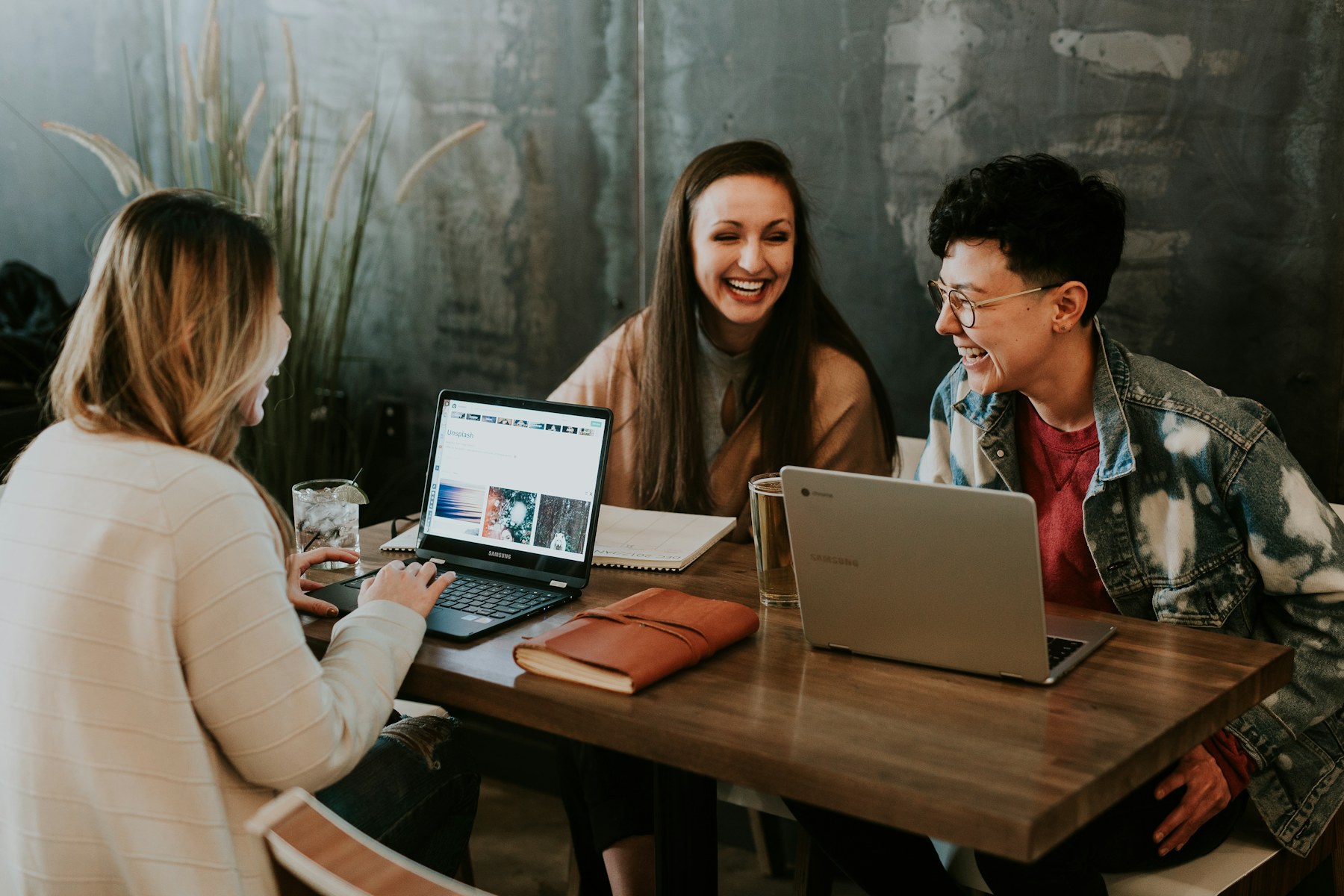 Three coworkers laughing around a table with laptops during a team check-in